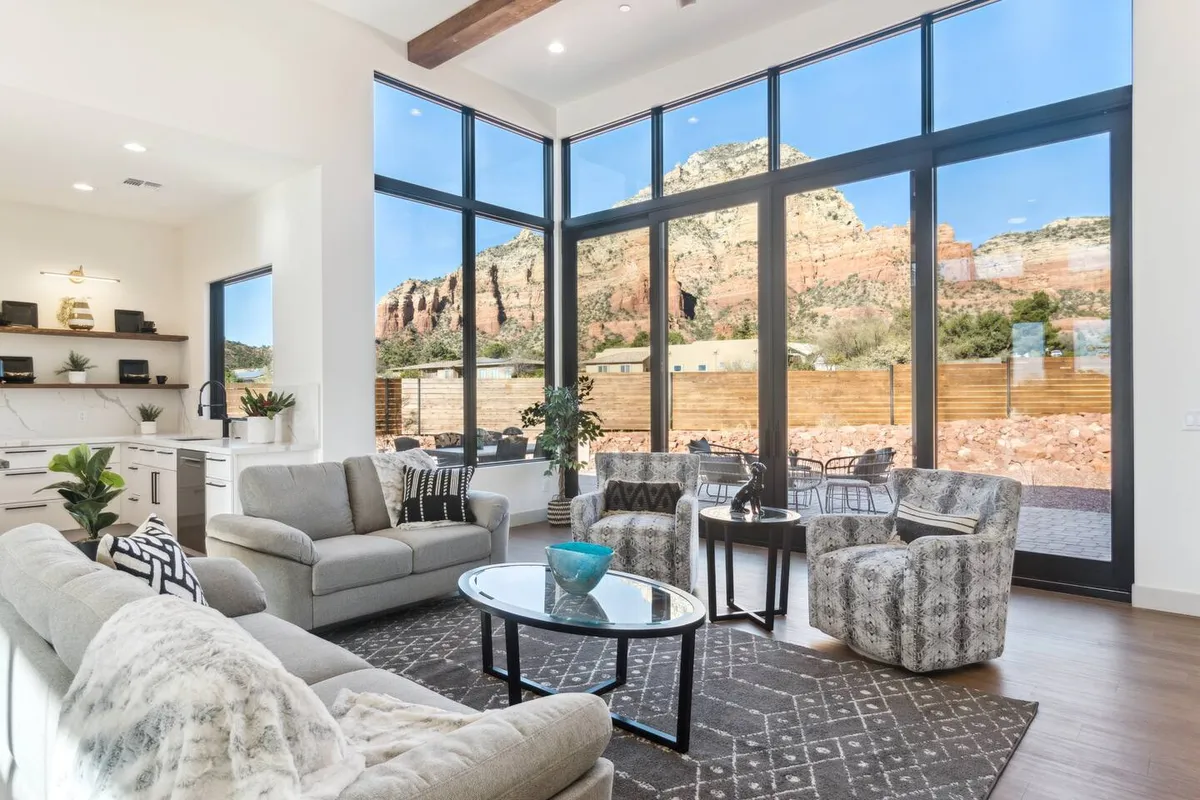 A spacious living room with large windows that frame panoramic mountain and red rock views. The seating arrangement is modern and stylish, with a decorative coffee table and comfortable chairs positioned to take in the stunning scenery. Natural light fills the room, enhancing the calming and open atmosphere.