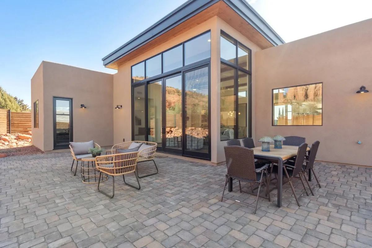 A welcoming outdoor dining area with large glass windows, wicker seating, and a dining table set for al fresco meals. The ambiance is friendly and inviting, with views of the surrounding landscape and soft lighting suggesting evening gatherings and intimate dinners.