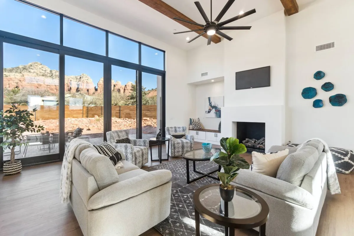 A chic, inviting living area featuring a large expanse of windows that offer mountain views. The modern furniture, stylish ceiling fan, and tasteful artwork create a space perfect for both relaxing and socializing, while sunlight pours in and emphasizes the open layout.