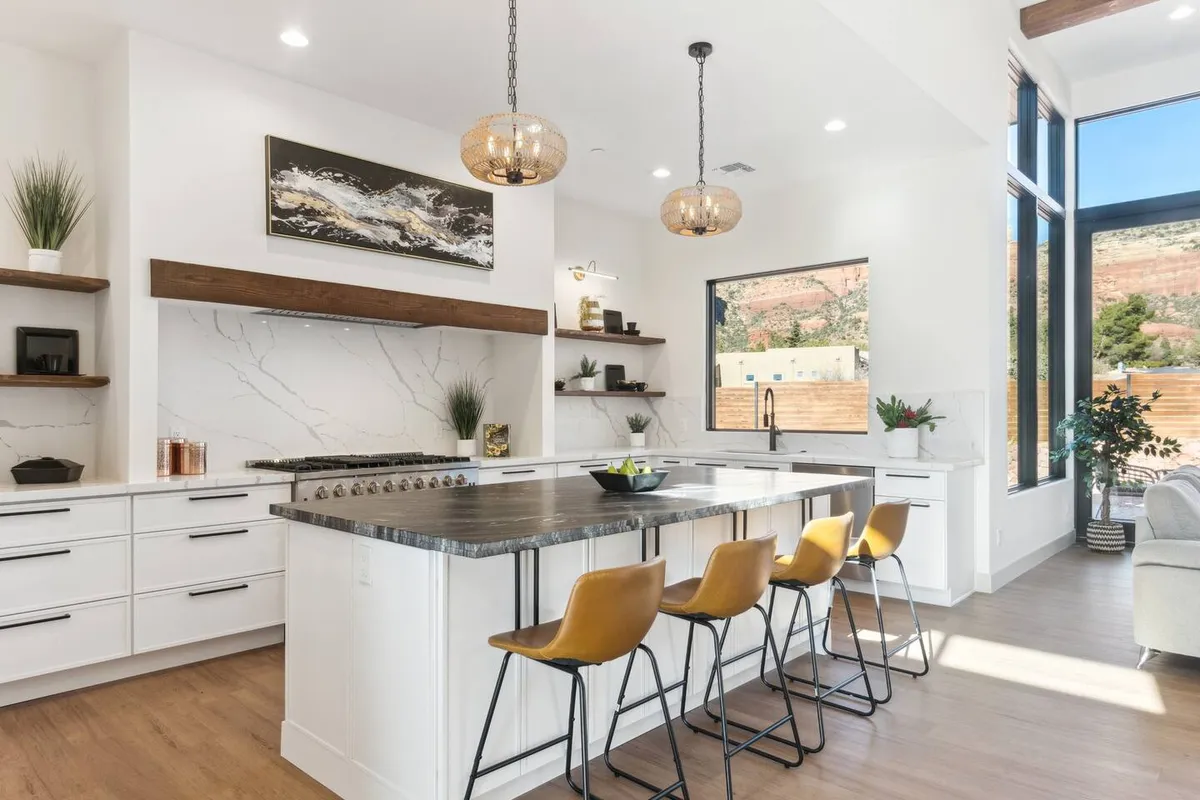 This bright kitchen highlights an island countertop, a state-of-the-art cooking range, large windows, and decorative artwork. The setting is vibrant and modern, suggesting a space where family and friends naturally come together for meals, celebrations, or simply to enjoy coffee with a view.