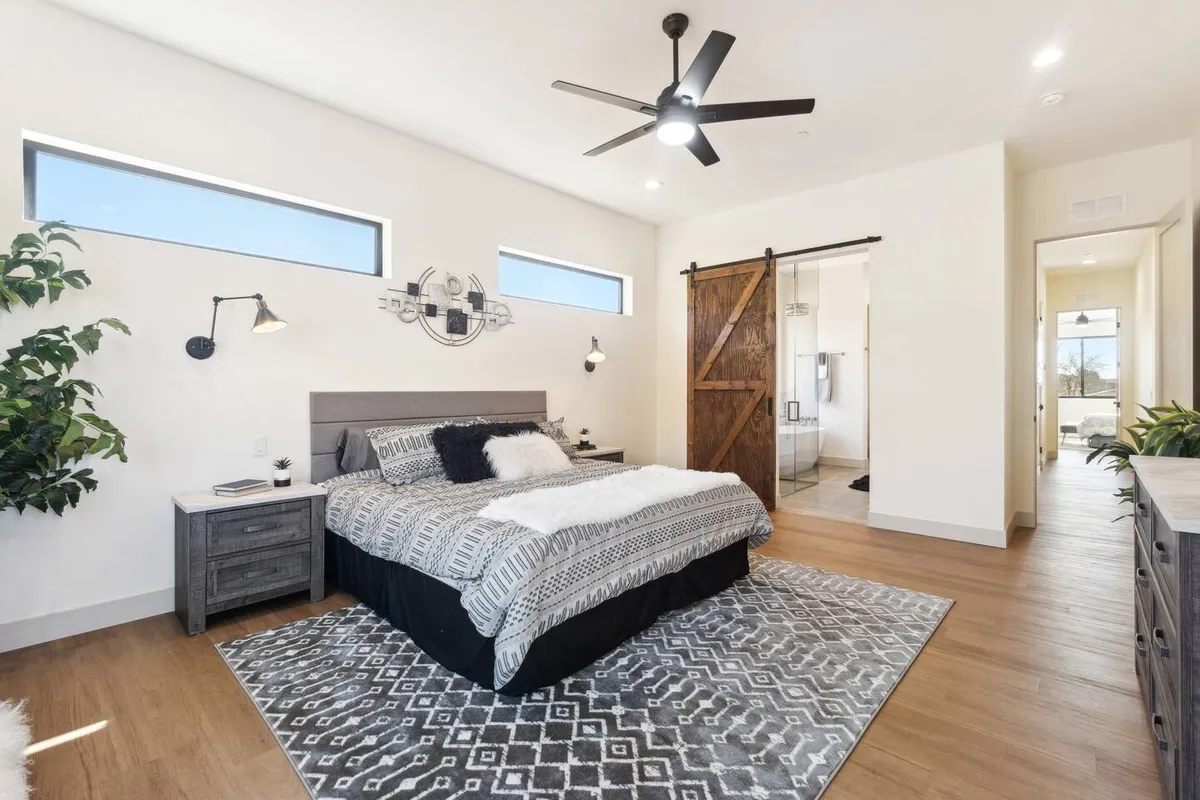 A contemporary bedroom with a plush bed, barn door accent, stylish lighting, an area rug, and touches of greenery. The space feels intimate and cozy, making it well-suited for couples or friends seeking a relaxing retreat. The combination of modern design and comfort elements enhances the sense of a private sanctuary.