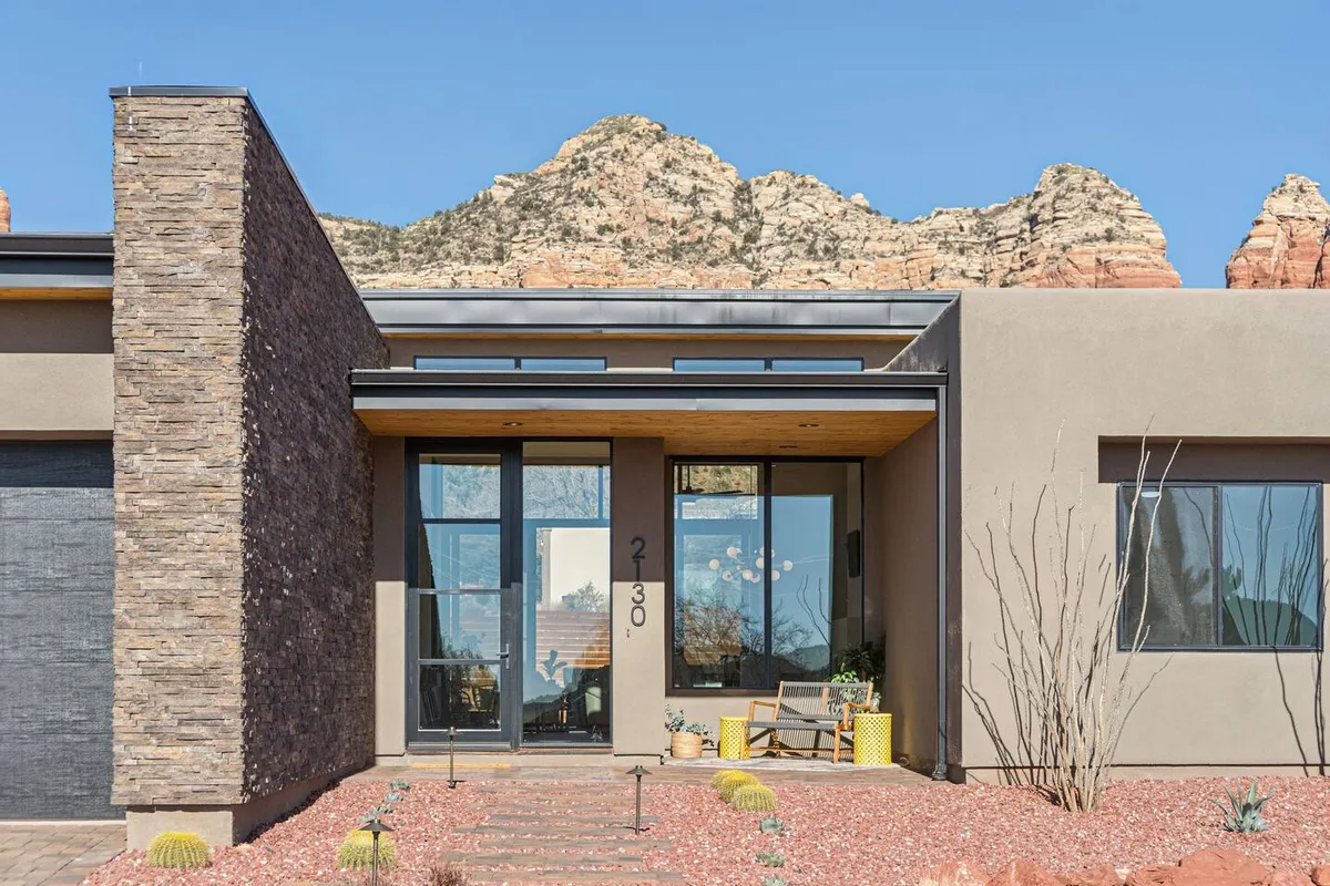 The modern stone facade of a home with a welcoming entrance and a dramatic mountain backdrop. The landscaped front yard provides a sense of arrival, while the natural scenery connects the home directly to Sedona’s outdoor appeal and walkability.