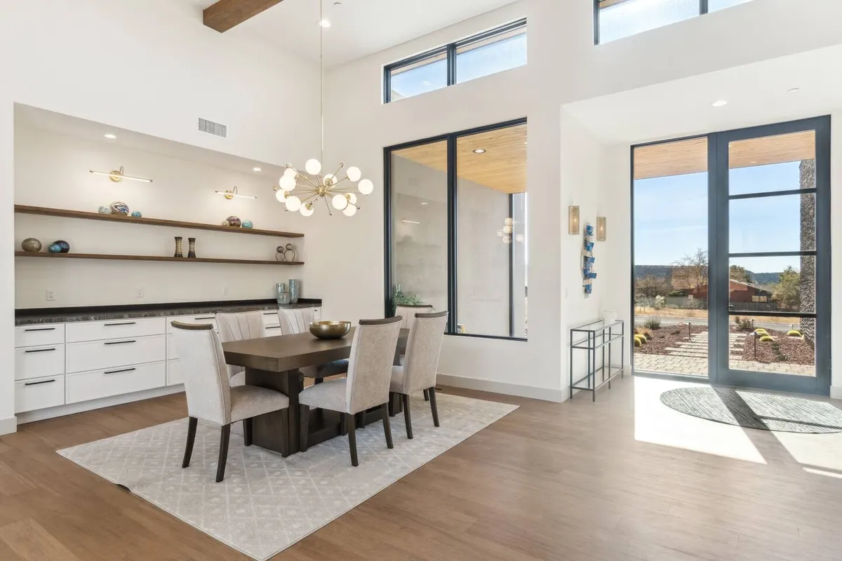 A dining area with a striking chandelier and large windows that let in natural light and frame beautiful outdoor views. The spacious table is set for gatherings, reflecting the seamless flow between living and dining spaces mentioned in the section.