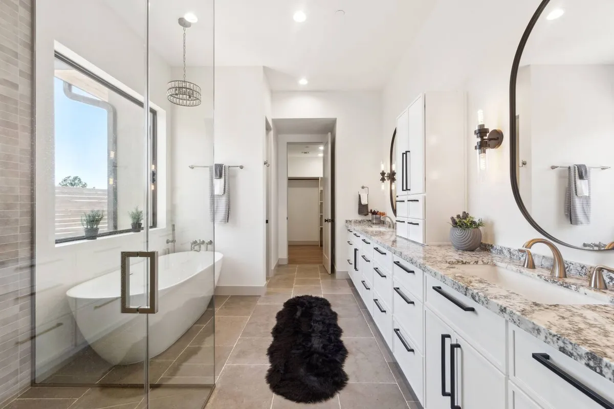 A spa-inspired bathroom with a freestanding bathtub, double sink vanity, large windows allowing in ample natural light, and chic lighting fixtures. The atmosphere is tranquil and luxurious, offering the ideal space for self-care routines and rejuvenation after a long day.
