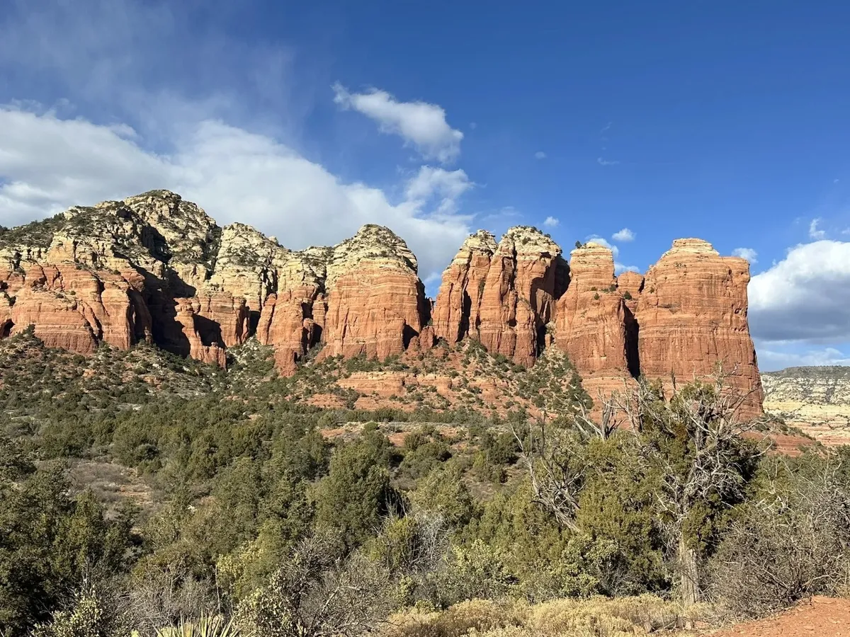A captivating view of dramatic red rock formations and distant mountains, framed by lush green shrubs. The lighting suggests sunset, bathing the scene in warm hues and showcasing the awe-inspiring natural environment surrounding the home.