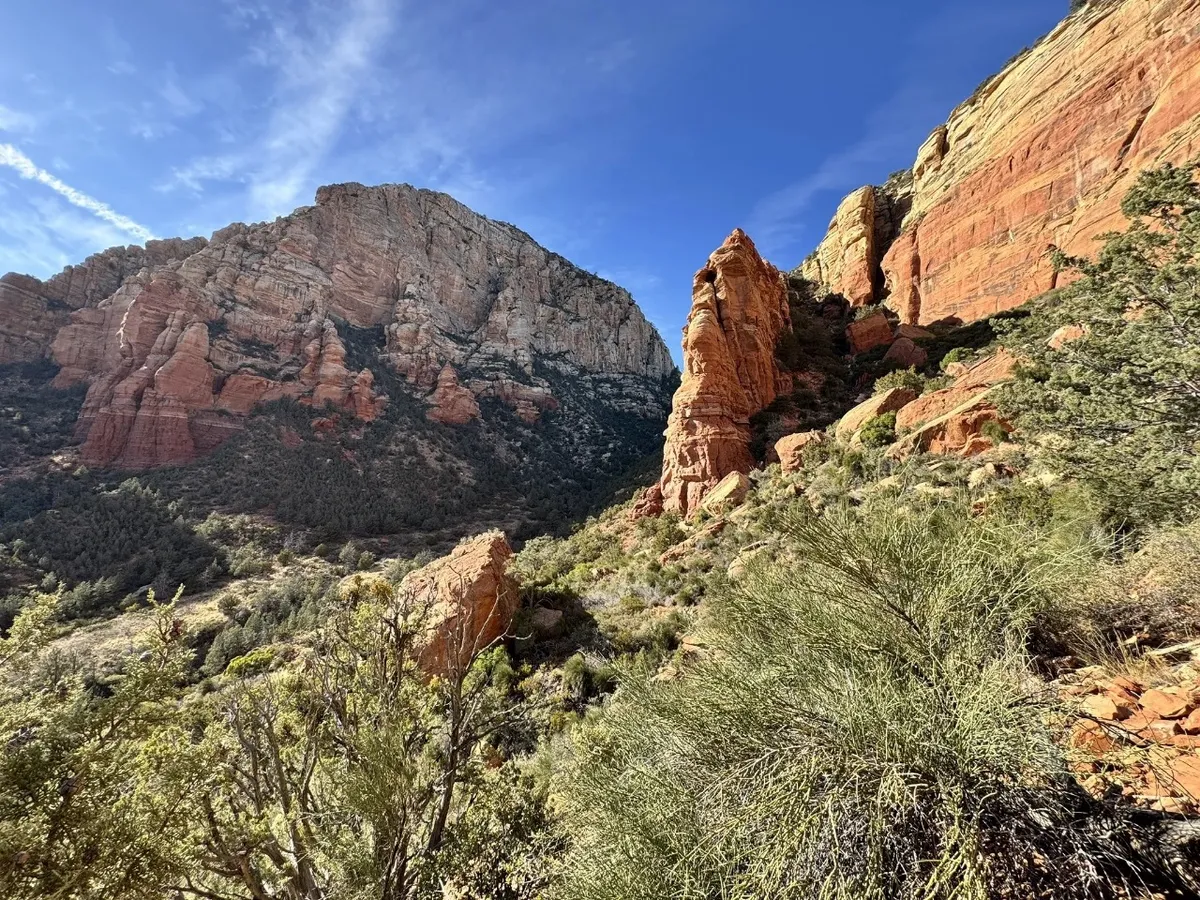 This exterior image captures dramatic red rock formations and a mountain backdrop, surrounded by lush vegetation. The setting embodies the iconic natural beauty of Sedona and is perfect for nature photography, hiking, and sunset watching.